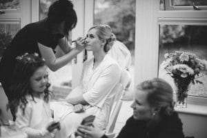 Bride having her make up being applied with a flower girl in the foreground