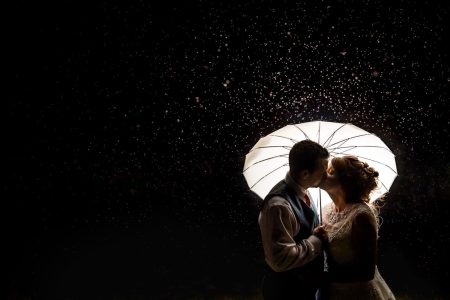 Winter Wedding Photography-35 In this enchanting winter wedding photograph, the bride and groom share a passionate kiss under an umbrella in the rain.