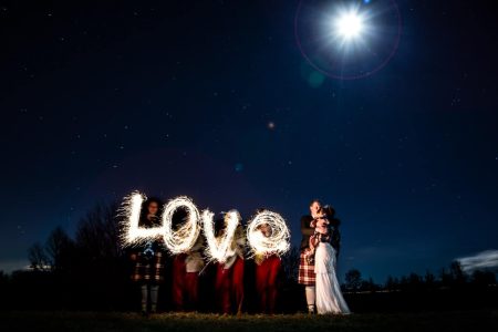 Winter Wedding Photography-5 A bride and groom holding sparklers under a full moon at their winter wedding.
