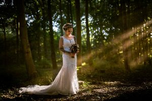beautiful ethereal photo of a bride in a wood in east hunsbury country park, with sun beams piecing the woodland canopy