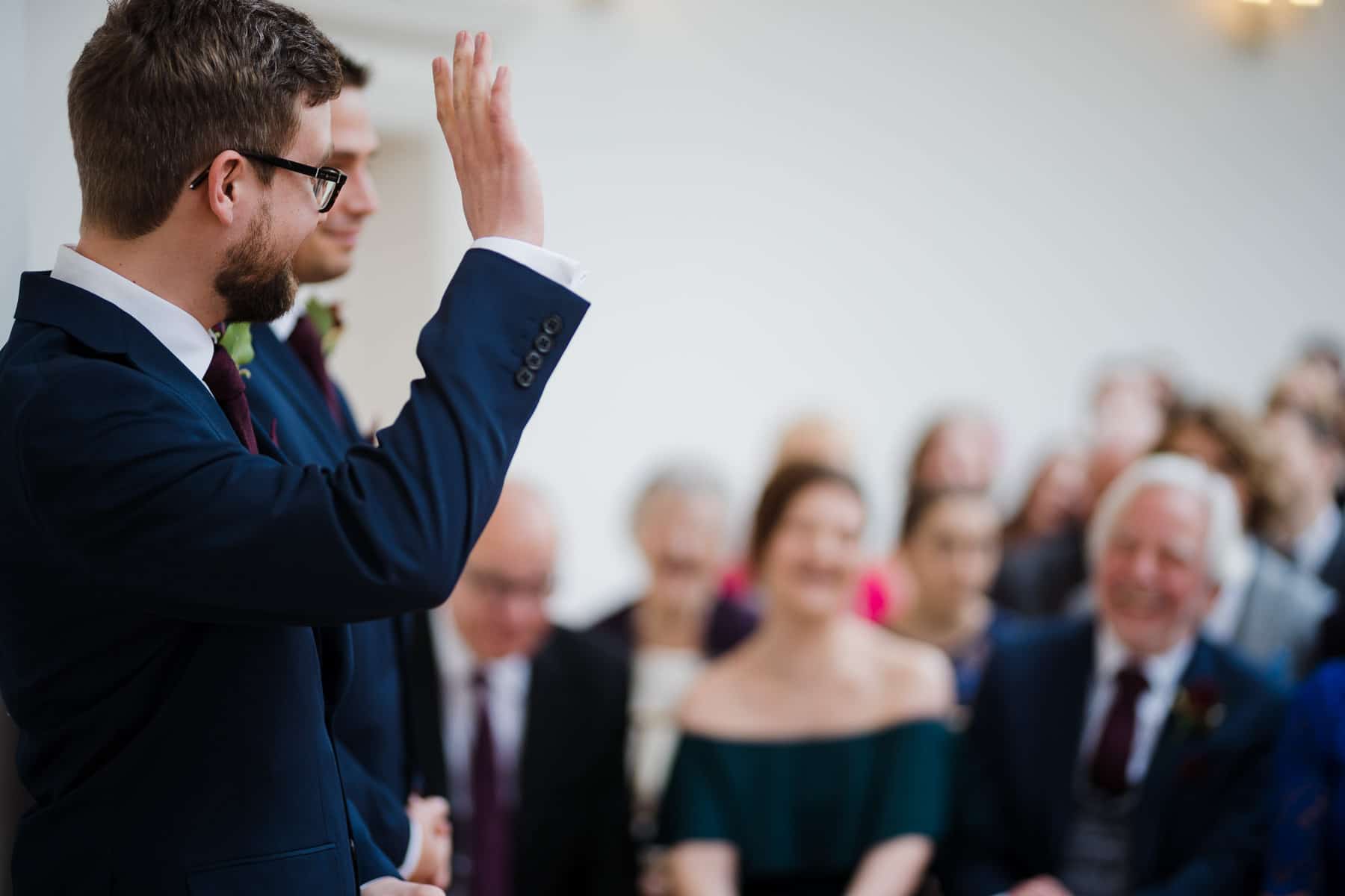 Groom waving goodbye to his wedding guests in the orangery barton hall