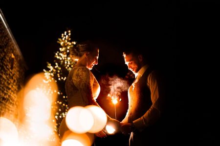 Off camera magmod photo Wedding Photographers capturing a bride and groom holding sparklers in front of a Christmas tree.