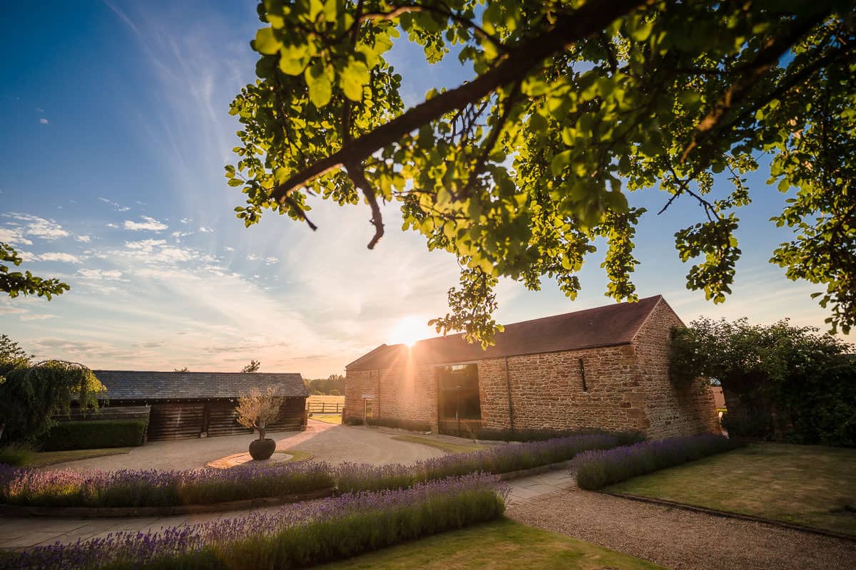 Dodford Manor Wedding Venue-6 A stone barn with lavender in front of it at sunset, captured beautifully by the Dodford Manor Wedding Photographer.
