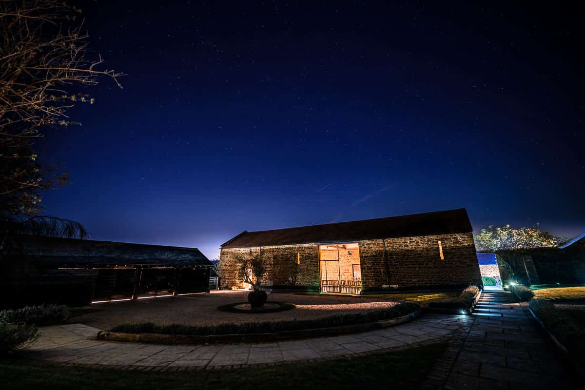 Dodford Manor Wedding Venue A stone barn at Dodford Manor lit up at night with a starry sky.