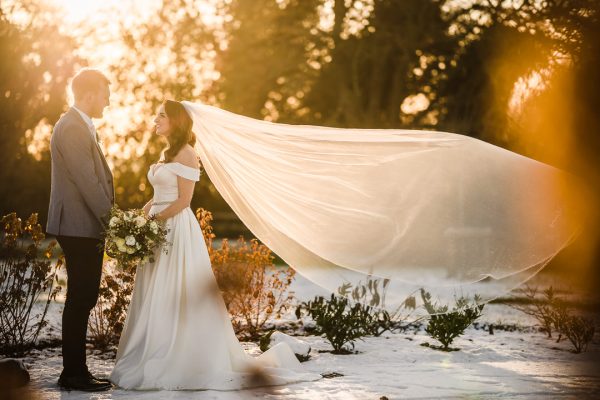 Featured Wedding-8 Bride and groom in sunlight, veil flowing.