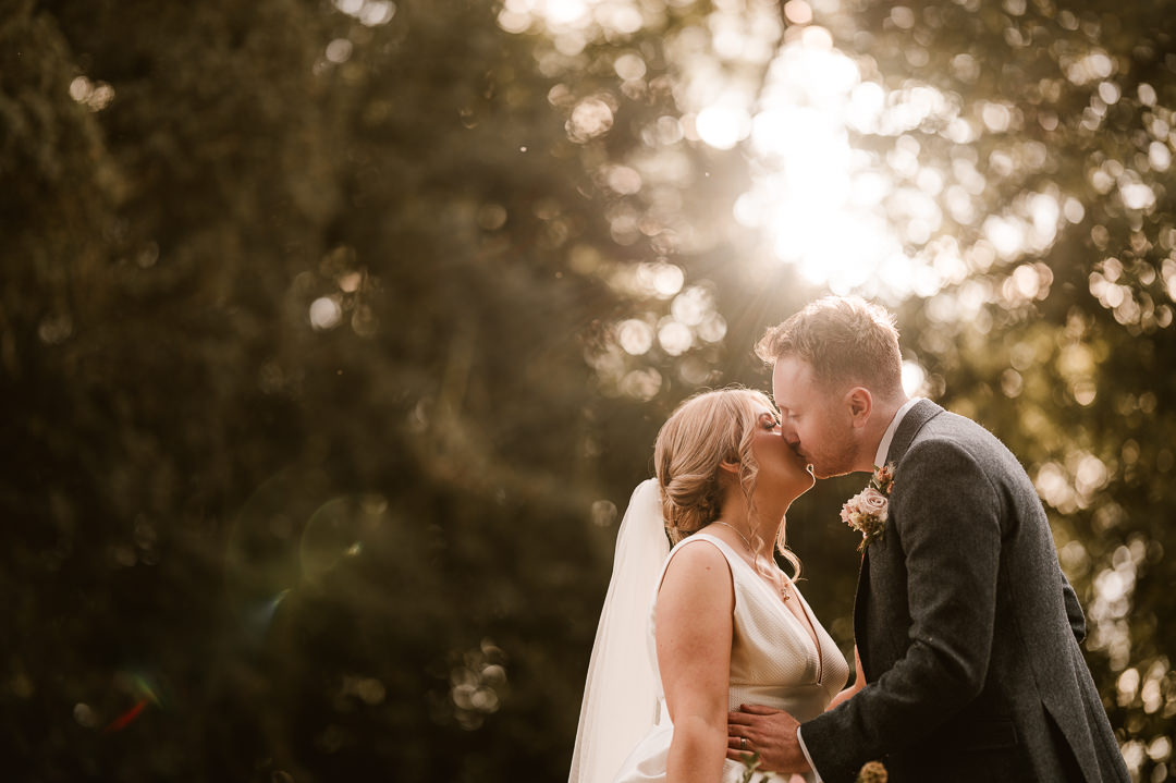 A Dodford Manor recommended photographer captures a romantic moment of a bride and groom kissing in the sun.