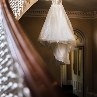 wedding photography portfolio 103 A white wedding dress hangs from a spiral staircase railing inside a building with ornate moldings and cream-colored walls.