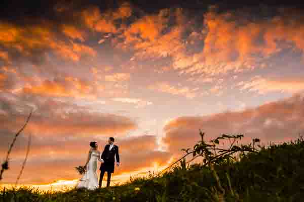 wedding photography portfolio 2 A couple in wedding attire stands on a grassy hill at sunset, captured in a stunning shot by a talented wedding photographer from Buckinghamshire. The dramatic, colorful sky above adds to the perfect romantic setting.