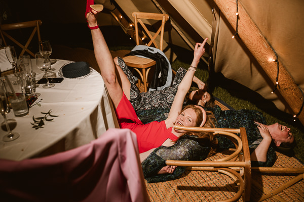 wedding photography portfolio 32 Three people lie playfully on the floor of a tent, surrounded by overturned chairs and a table with empty glasses—a perfect scene for any Warwickshire Wedding Photographer to capture the joy and spontaneity of the moment.