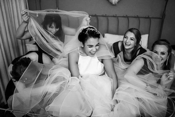 wedding photography portfolio 4 Five women laughing playfully under sheer veils on a bed, captured perfectly by a Warwickshire wedding photographer.