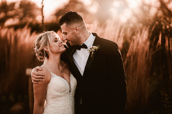 wedding photography portfolio 43 A couple in formal attire embraces outdoors at sunset, surrounded by tall grass, with the moment beautifully captured by a Warwickshire wedding photographer.