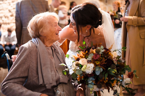 wedding photography portfolio 63 A bride in a white dress and veil smiles warmly at an elderly woman in a wheelchair. The bride holds a bouquet of flowers.