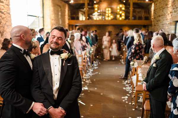 wedding photography portfolio 65 A groom stands smiling with a friend in a rustic wedding setting, as guests seated in rows look on.