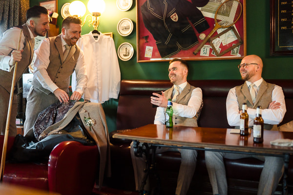 wedding photography portfolio 74 Groomsmen preparing, laughing in vintage-themed room.