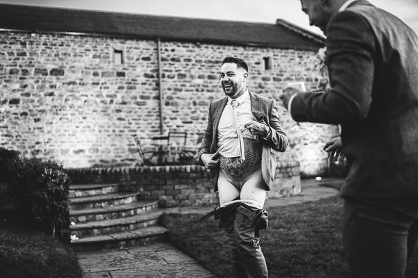 wedding photography portfolio 8 A man outdoors, laughing with his pants down, stands before a stone building in Warwickshire, captured by a wedding photographer.