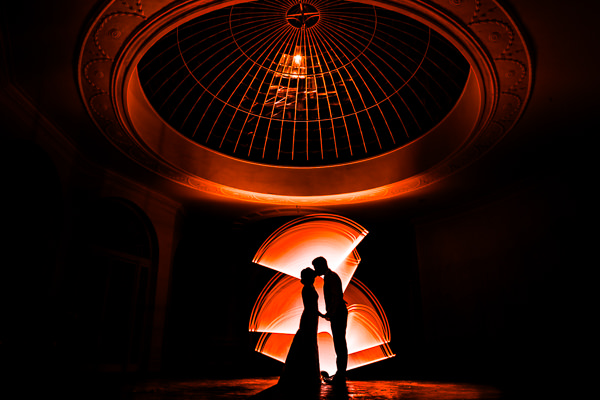 winter low light wedding photographer 2 Silhouette of a couple embracing under a large, round ceiling with glowing orange light trails in the background.