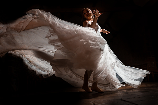 winter low light wedding photographer 21 Person in a flowing white dress spins joyfully on a dimly lit floor, creating a dramatic motion effect.