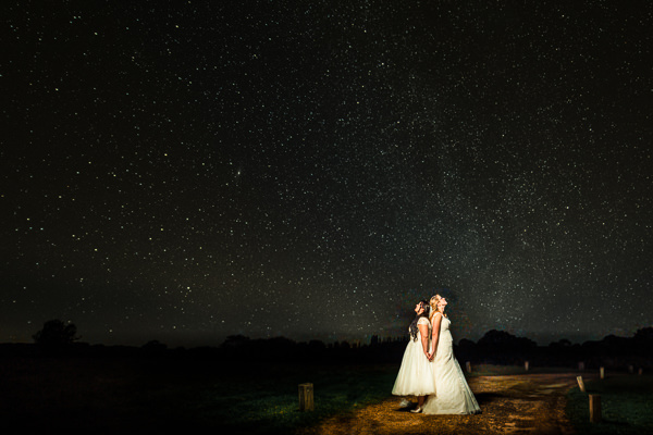 winter low light wedding photographer 22 Two brides hold hands, standing on a path under a starry night sky, captured beautifully by Winter Wedding Photographers in Warwickshire.