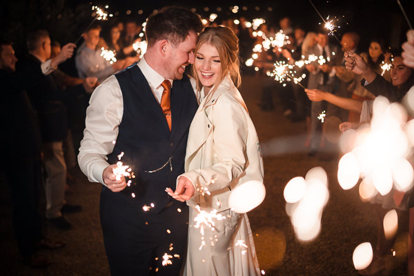 winter low light wedding photographer 32 A couple celebrates with sparklers, surrounded by guests at a nighttime gathering captured beautifully by a Milton Keynes wedding photographer.