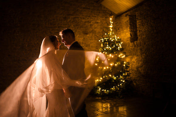 winter low light wedding photographer 36 Bride and groom embrace near Christmas tree.
