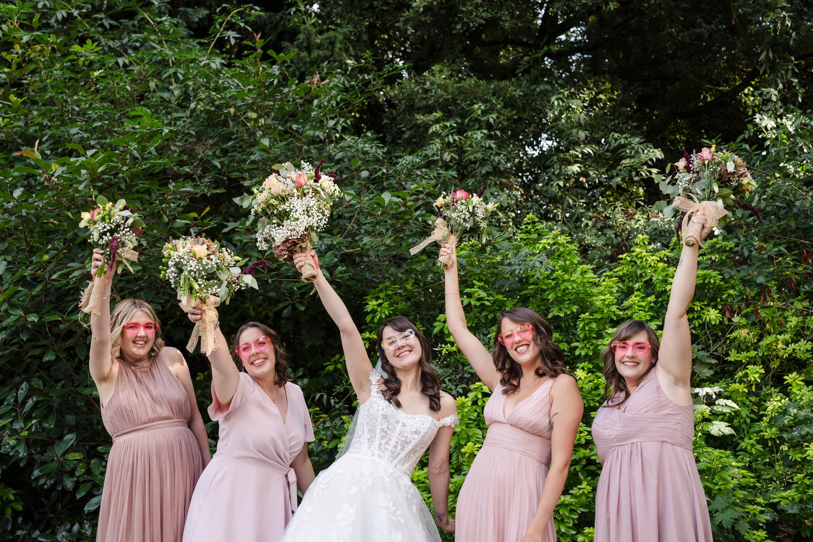 Bridesmaids in pink dresses holding flower bouquets outside.