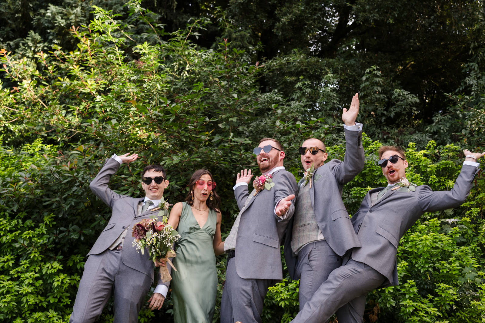 Wedding party posing playfully outdoors in suits and dress.