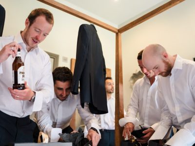 benefits of two photographers 26 A group of men in white shirts busily prepares, one clutching a bottle while a jacket hangs in the background. This lively scene highlights the benefits of a second photographer capturing every candid moment.