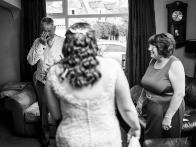 bride getting ready 16 A man wipes his eyes in a living room, facing a woman in a dress and the bride, who is preparing for her big day. Two photographers expertly capture this intimate moment, with a second shooter documenting every detail of the bride getting ready.