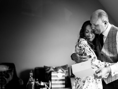 bride getting ready 25 A man and woman share a heartfelt hug while she holds a card, beautifully capturing the emotion before the bride gets ready for her big day. In the background, gift bags and a chair quietly witness this tender moment.