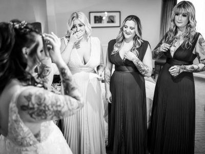 bride getting ready 27 In a black and white scene, the bride, getting ready with her three bridesmaids in long dresses, observes their varied reactions. Meanwhile, two photographers capture groom and bride preps from different angles to ensure every moment is perfectly documented.