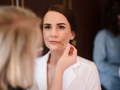 bride getting ready 31 A woman in a white shirt is having makeup applied by another person holding a brush, as two photographers capture the bride getting ready, ensuring no detail goes unnoticed.