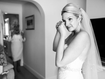 bride getting ready In a room filled with anticipation, a bride in a white gown wipes her eyes as two photographers capture the magic of her getting ready, while another woman looks on in the background.