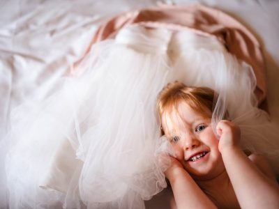 bride getting ready 42 A child smiles and plays under a sheer white fabric, with layered fabric resembling a dress in the background, as two photographers capture the joyful moments akin to a bride getting ready.