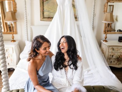 bride getting ready 46 In a room with ornate decor, a second shooter captures two women sitting on a bed. One in a light blue dress and the other in a white robe, they share smiles, reveling in the bride getting ready for her big day.