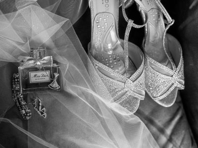 bride getting ready details 2 Black and white image of glittery high heels, a Miss Dior perfume bottle, earrings, bracelet, and tulle fabric arranged decoratively.