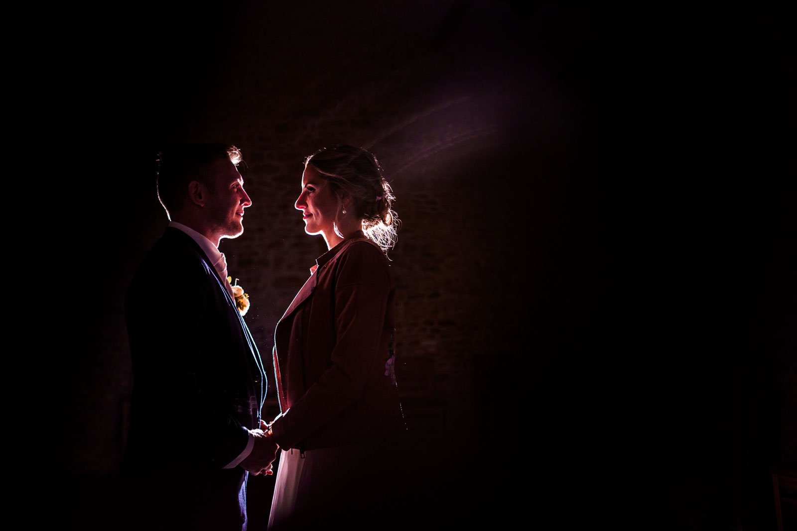 Silhouetted couple holding hands and facing each other in a dark setting with light illuminating their profiles.