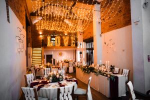 Discover the enchanting ambiance of Dodmoor House, a Northamptonshire venue, where beautifully decorated tables and arranged chairs meet hanging string lights. Capture every detail with Dodmoor House wedding photography amidst the elegant mezzanine and charming brick walls.
