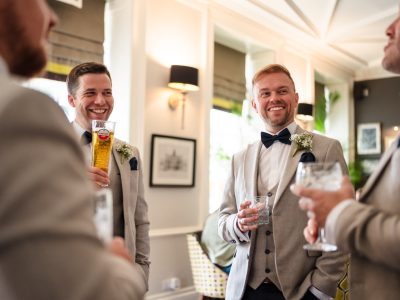 second photographer shots 22 Four men in light gray suits and bow ties are smiling and holding drinks in a well-lit, elegantly decorated room, capturing a perfect moment of groom prep photography.