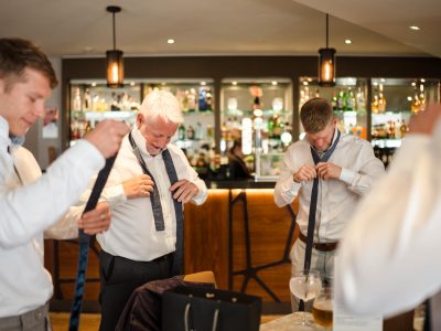 second photographer shots 26 Four men in a bar area, wearing shirts and adjusting neckties, with drinks on a table nearby—a perfect scene for groom prep photography.
