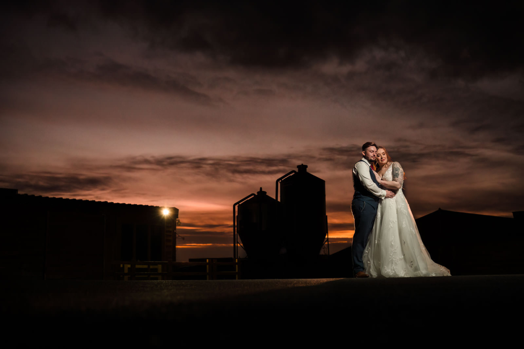 A couple embraces on a rooftop at sunset, with an industrial background providing unique winter wedding photography ideas.