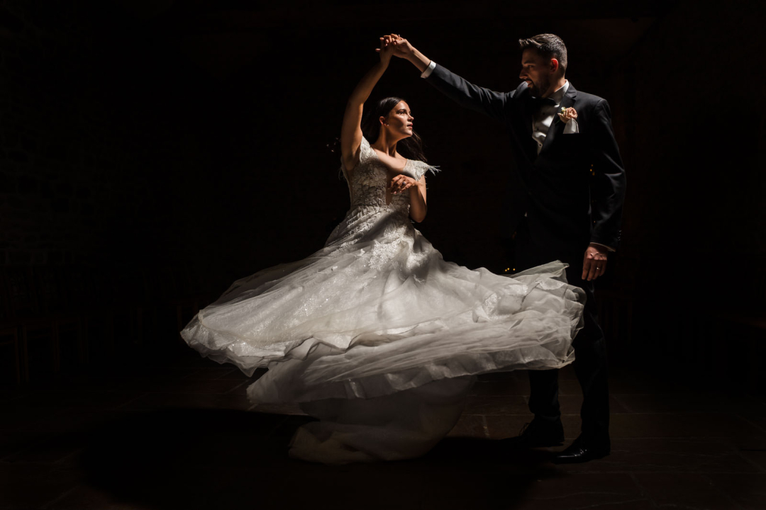 A bride and groom dance gracefully, her gown swirling in motion against a dark winter backdrop, captured perfectly by a talented wedding photographer.